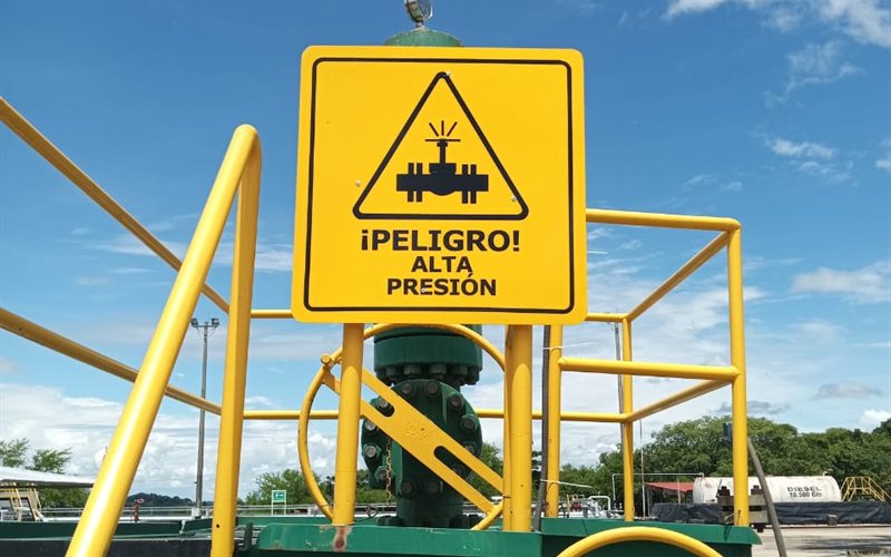 Letrero amarillo de peligro por alta presión instalado sobre una válvula en una planta industrial